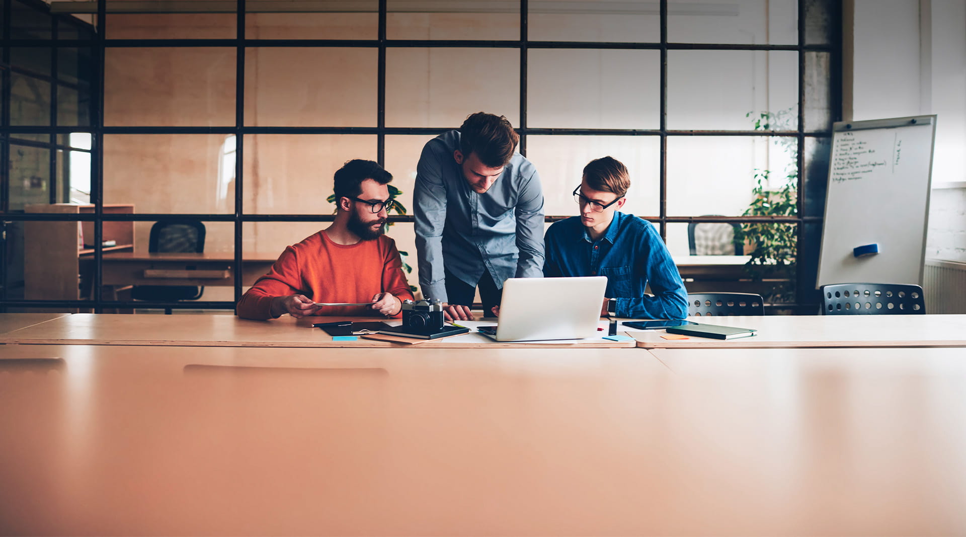 Three persons looking at laptop screen in boardroom