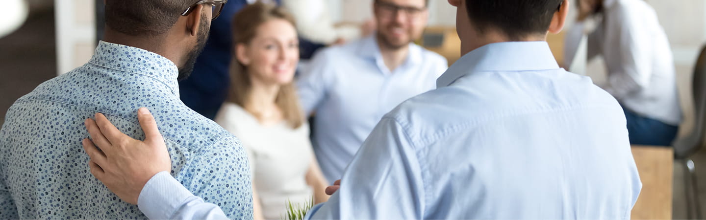 Person with hand on back of another facing group of persons in office