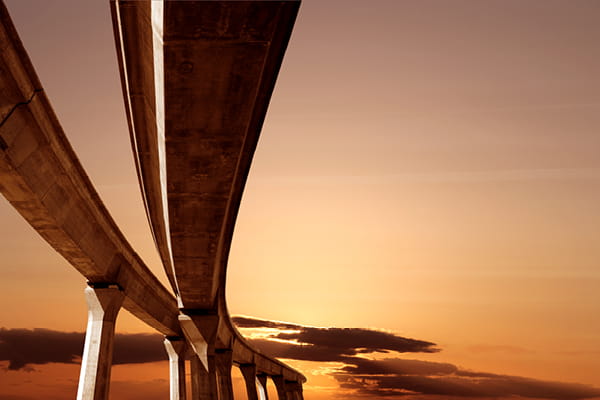 A bridge silhouetted against a vibrant sunset, with warm hues of orange and pink filling the sky.