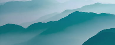 Layered blue-green mountain ridges receding into misty haze under a serene sky.