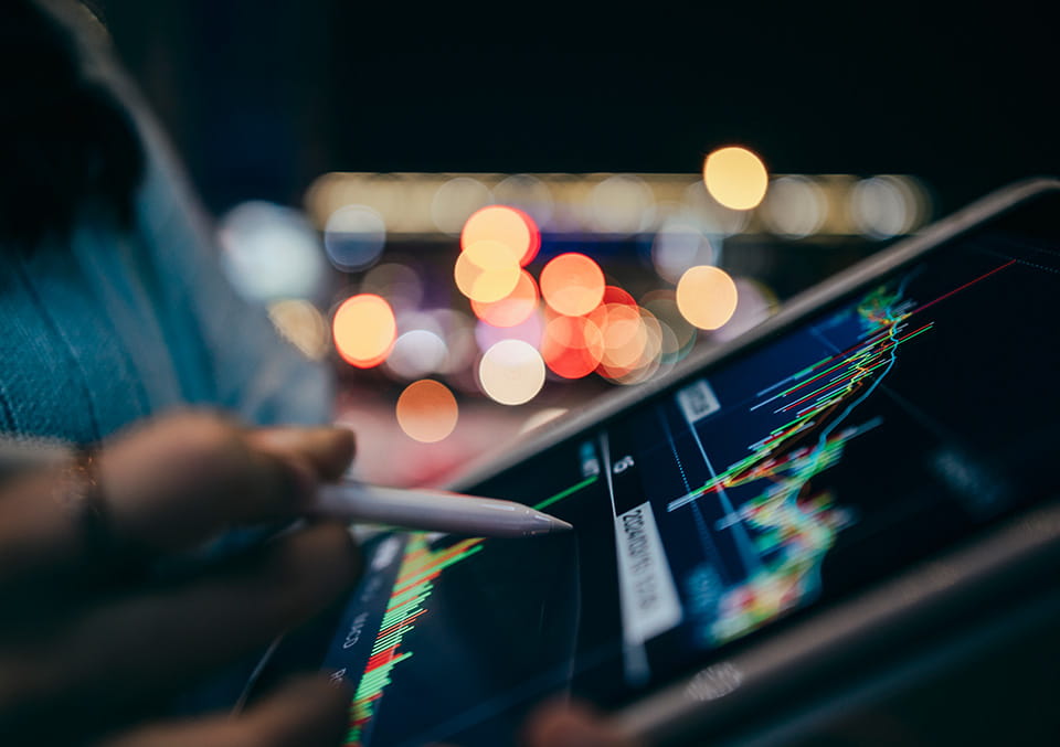 Hands holding a tablet with a stylus, displaying financial trading charts. Used in the private capital call series.
