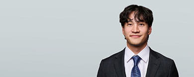 Headshot of summer clerk Matthew Vermeulen, in a dark checked suit and blue tie, against a grey backdrop.