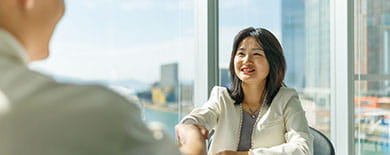 Two professionals shaking hands in a modern high-rise office overlooking Hong Kong's harbor and city skyline