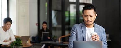 Young professional working on a laptop in a modern co-working space with large windows and greenery