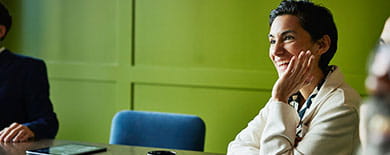 Smiling woman in a cream blazer engaged in a meeting in a conference room with green paneled walls