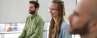 Three colleagues smiling during a casual meeting in a bright office with whiteboards in the background