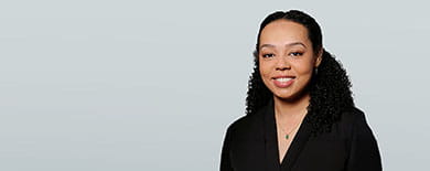 Professional headshot of a smiling young woman with curly black hair wearing a black blazer