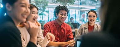 Group of young professionals smiling and collaborating around a white table in a modern office with plants