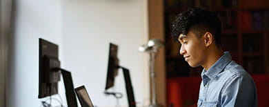 Young man in a light blue denim shirt working on a laptop at a desk in a warm, book-lined office environment