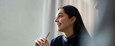 Young woman in a navy blouse smiling in profile while holding a pen during a meeting in a softly lit office