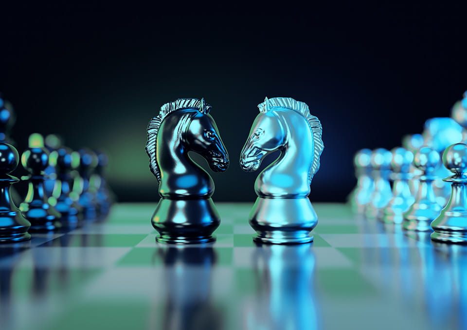 Two metallic knight chess pieces face off on a green chessboard
