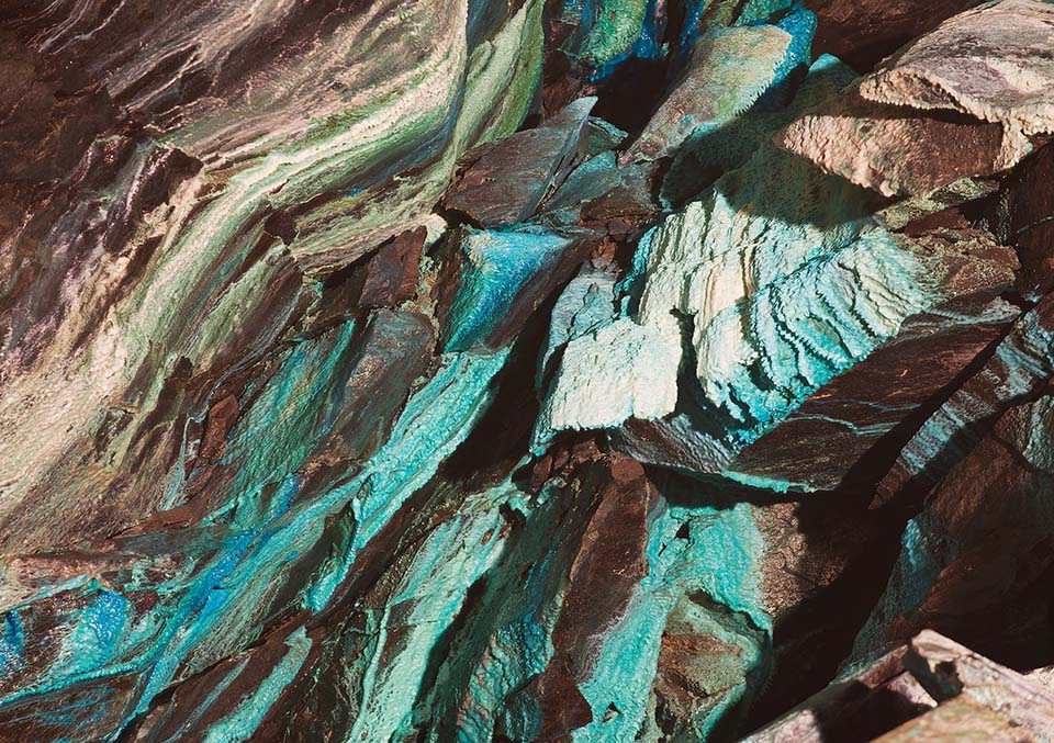 Close-up of turquoise and brown layered rock formation with copper mineral deposits and natural geological textures