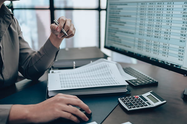 Employee reviewing a spreadsheet at a desk with a calculator, binder and paperwork. 