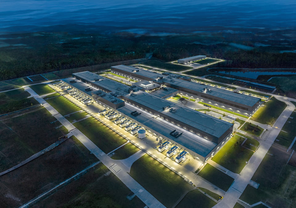 Aerial night view of a large, brightly lit data center campus with rows of backup generators