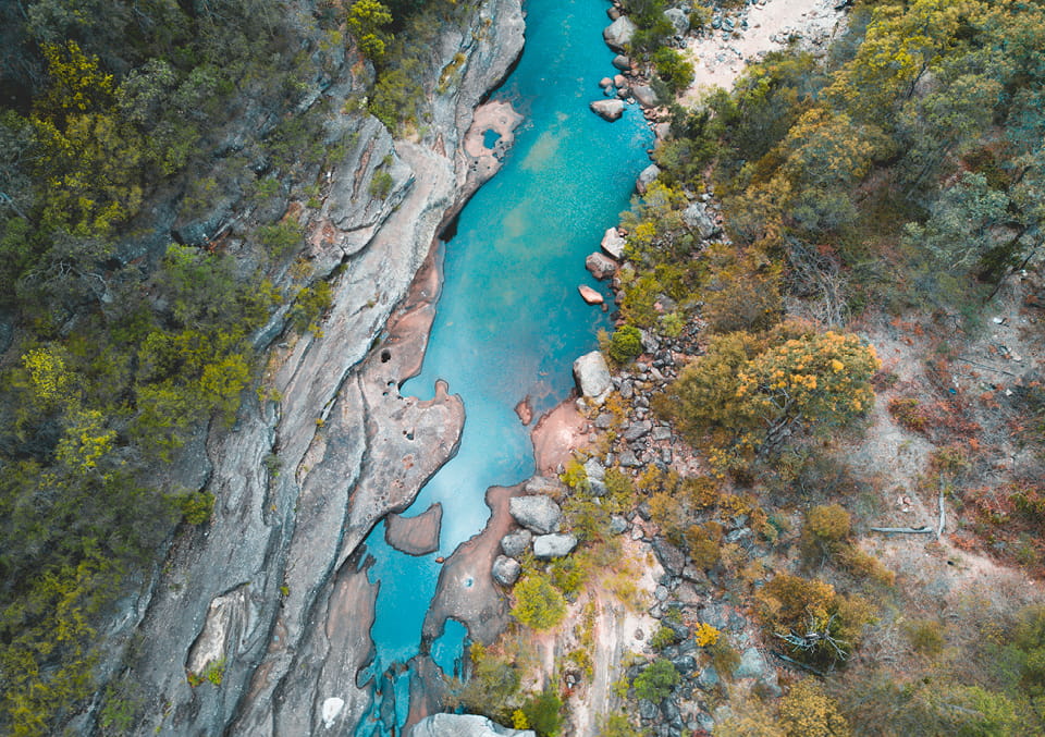 Aerial view looking straight down on a turquoise river flowing through a narrow rocky gorge lined with vegetation.