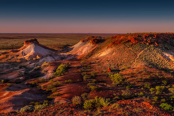 Eroded outback mesas with red, white and ochre rock bands above a vast plain at twilight.