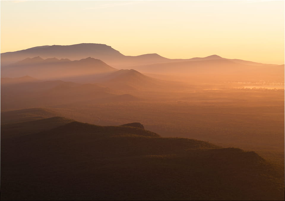 Layered mountain ridges fading into golden haze at sunrise, seen from a high vantage point.