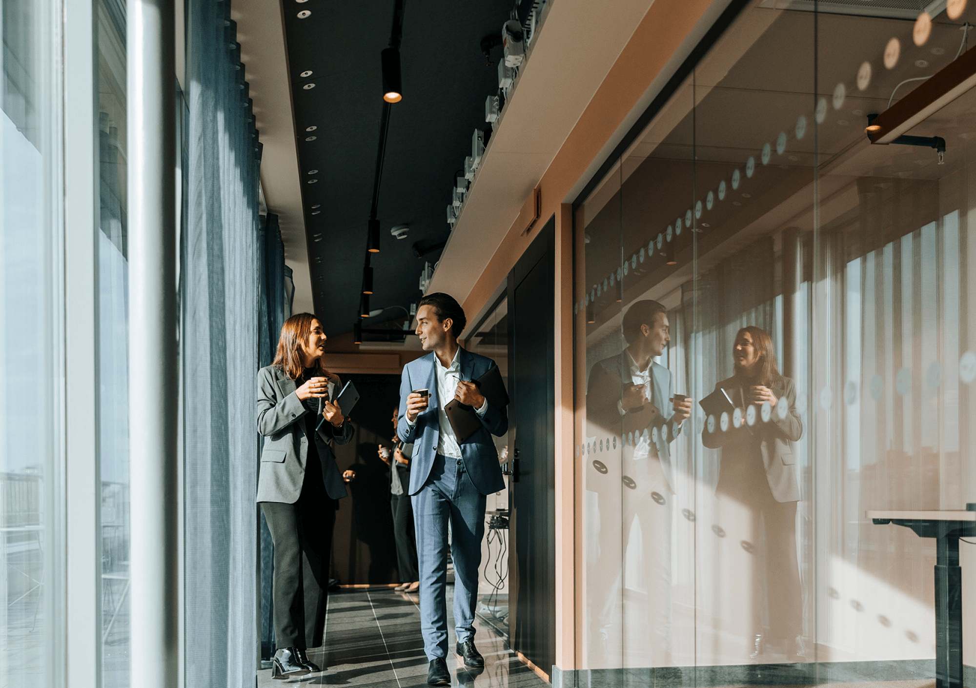 Two colleagues chatting while walking through a modern glass-walled office corridor
