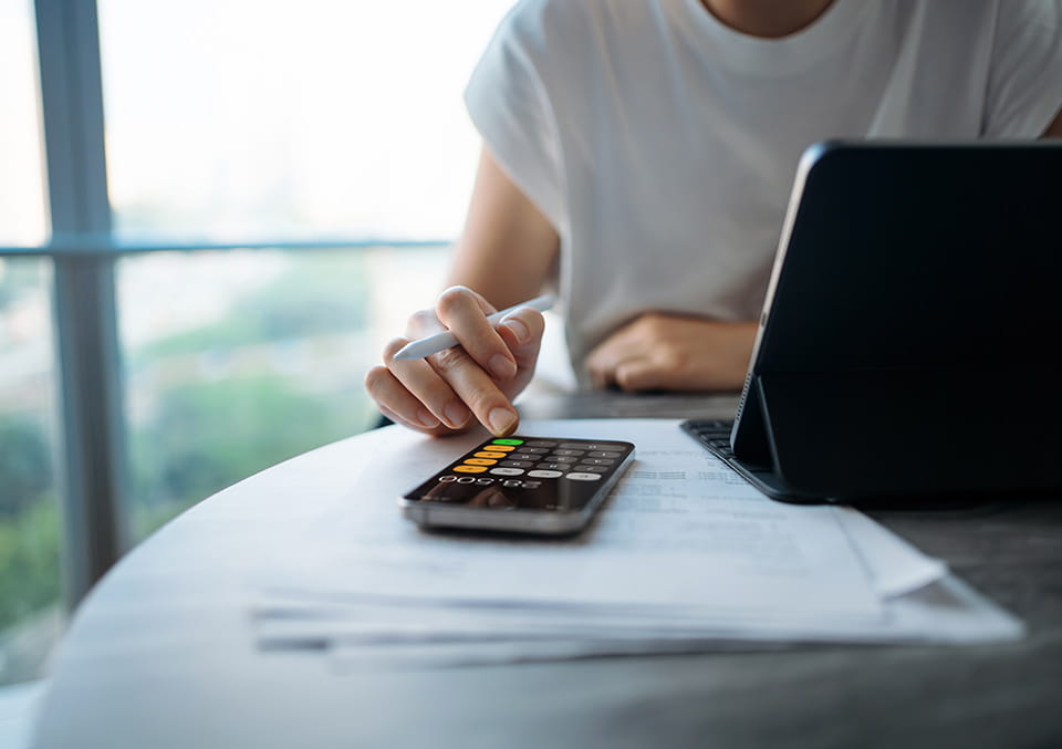 	Business professional's hand holding a pen near a calculator at a desk by a window, financial services concept