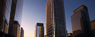 Modern city skyline with glass high-rise buildings bathed in warm golden sunset light against a deep blue twilight sky.