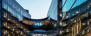 Two modern glass office buildings connected by curved sky bridges, photographed at dusk with warm interior lighting.