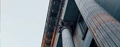 Low-angle view of a neoclassical building facade with grand fluted columns and an ornate cornice in warm sunlight