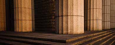Low-angle view of sunlit neoclassical stone columns and wide steps of a courthouse-style building