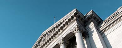 Neoclassical courthouse facade with Corinthian columns and sculptural pediment against a clear blue sky.