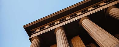 Sandstone courthouse columns lit by golden afternoon sunlight, viewed from a low upward angle