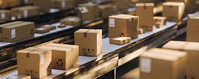 Cardboard shipping boxes with handling symbols on warehouse conveyor belts in warm amber lighting.