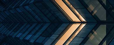 Symmetrical modern building interior with angular steel and glass converging toward a golden light.