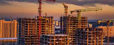 Large construction site with tower cranes and concrete high-rises under a dramatic golden sunset sky.