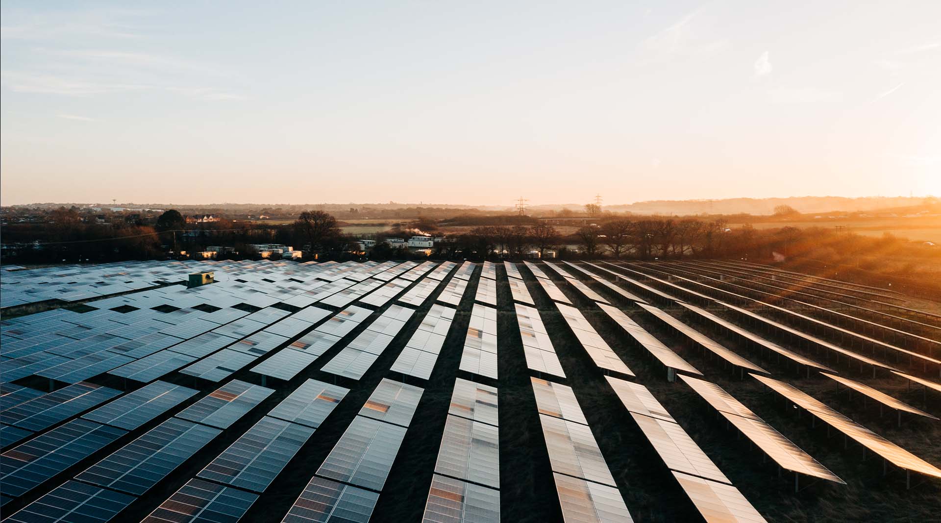 Aerial view of a vast solar panel farm stretching to the horizon under a golden sunrise sky.